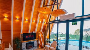 Um interior moderno com lareira, sinal da Netflix, vista para piscina e vigas de madeira.