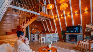 Uma sala de estar acolhedora em estilo loft, com decoração em madeira, uma televisão e uma escada que dá acesso a um andar superior.
