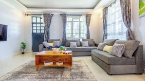 A living room with a sofa, a coffee table, and a television on the wall. - The Cabin Azure (Naivasha)