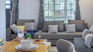 A modern living room with a grey sofa set, a wooden dining table, and a window with curtains. - The Cabin Azure (Naivasha)