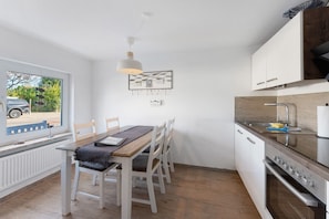 A modern kitchen with white cabinetry, a wooden dining table, and a hanging light fixture.