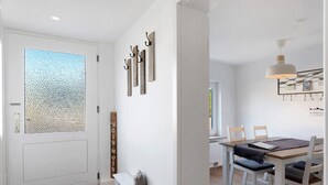 A modern interior with a white door, a bench, a dining table with chairs, and wall-mounted hooks. - Holiday Home 'Küstenliebe' with Private Terrace, Private Garden and Wi-Fi (Fehmarn)