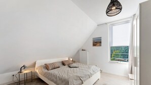 A bedroom with a bed, bedside lamp, radiator, window, and a view of greenery. - Holiday Home 'Küstenliebe' with Private Terrace, Private Garden and Wi-Fi (Fehmarn)
