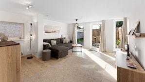 A modern living room with a sectional sofa, a standing lamp, and a wooden coffee table. - Holiday Home 'Küstenliebe' with Private Terrace, Private Garden and Wi-Fi (Fehmarn)