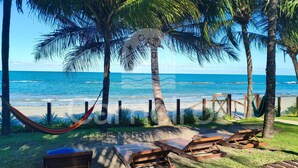 Vista de la playa con palmeras, una hamaca y sillones de madera.