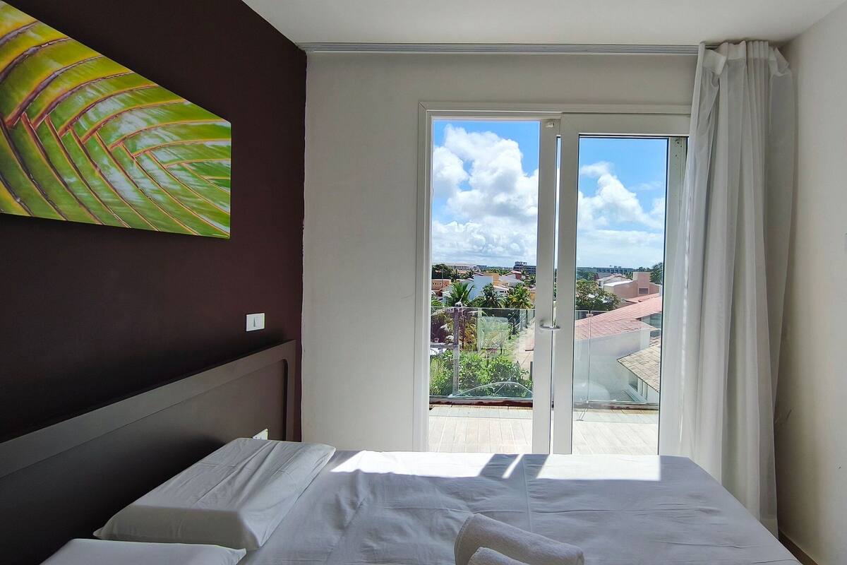 Une chambre avec un lit, une vue sur la ville à travers une porte vitrée et un tableau accroché au mur.