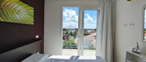 Un dormitorio con una cama, vistas de la ciudad a través de un ventanal y un cuadro en la pared.