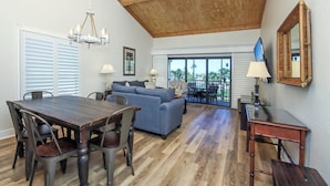 A spacious living area with a wooden ceiling, a dining table with chairs, a blue sofa, and a balcony with outdoor furniture. - Beach Villa 2121: Your Exclusive Two-Story Beach Villa with Direct Gulf Views (Captiva)