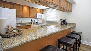 A kitchen with granite countertops, wooden cabinets, a microwave, a stove, and a coffee maker. - Beach Villa 2121: Your Exclusive Two-Story Beach Villa with Direct Gulf Views (Captiva)