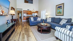 A spacious living room with a large TV, a sofa set, a coffee table, and a kitchen in the background. - Beach Villa 2121: Your Exclusive Two-Story Beach Villa with Direct Gulf Views (Captiva)