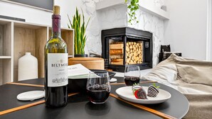 A modern living room with a fireplace, a bottle of Biltmore Estate Merlot, two glasses of red wine, and a plate with chocolate strawberries.