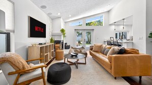 A modern living room with a sofa, armchair, coffee table, and a TV displaying 'NETFLIX'.