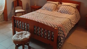 Une chambre à coucher avec un lit en bois, une table de chevet, une chaise et un petit tabouret.