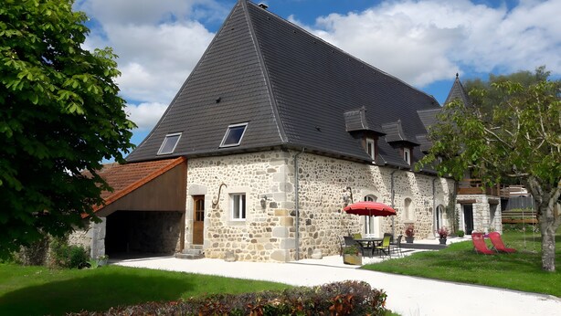 Un bâtiment en pierre avec un toit en pente, un patio couvert avec des chaises et un petit jardin.