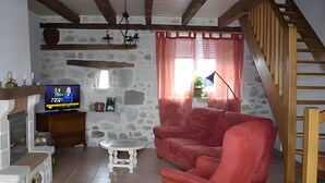 Un salon avec un mur en pierre, un téléviseur, un canapé rouge, une table basse blanche et un escalier en bois.