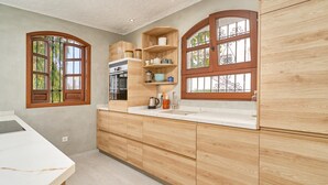 Uma cozinha com armários de madeira, bancada de mármore e janela com vista para árvores.
