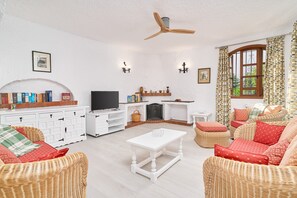 Een woonkamer met rieten meubels, een witte salontafel, een open haard en een televisie.
