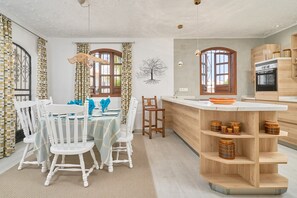 Een moderne keuken met een centraal eiland, houten kastjes en een eetgedeelte met witte stoelen en een tafel.