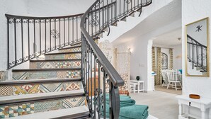 Uma escadaria com grades elaboradas e azulejos estampados, que leva a um espaço com área de refeições e um espelho na parede.
