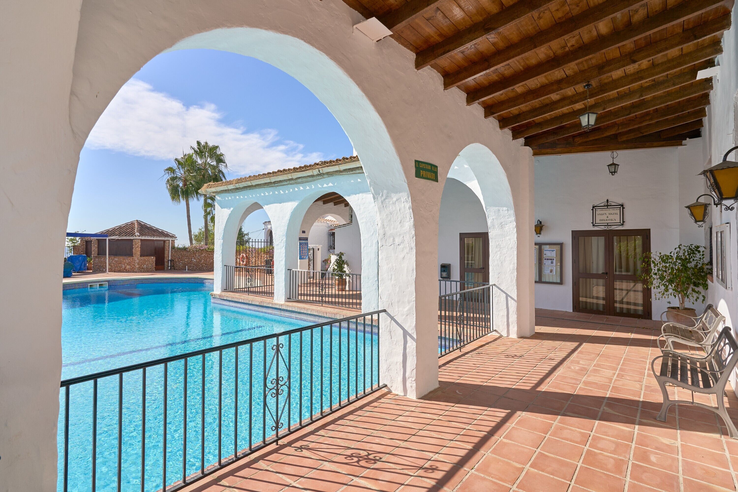 Una piscina amb un solàrium enrajolat, arcs blancs i un sostre de fusta.