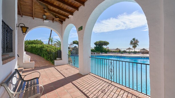 Uma área externa coberta com um banco, piscina e vista para a paisagem ao redor.
