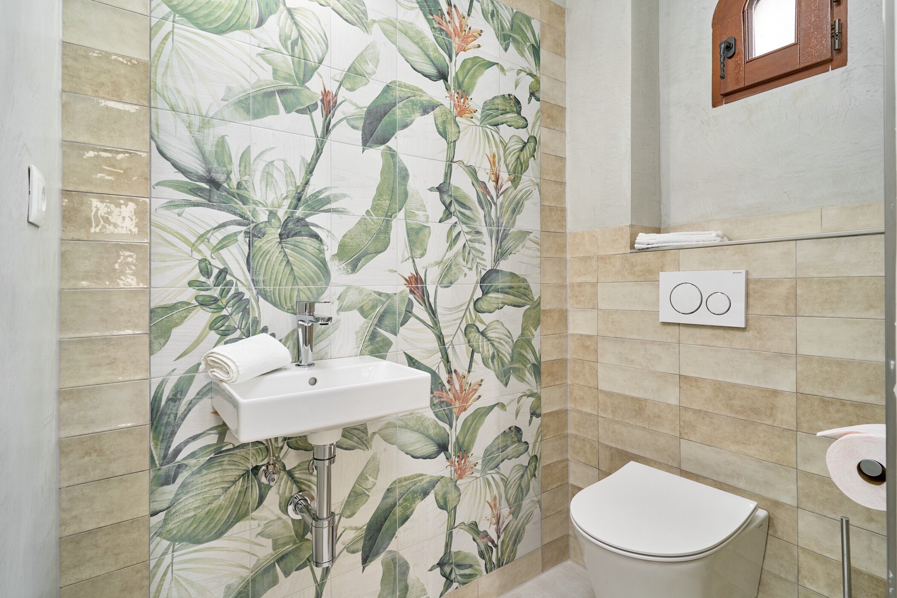 A bathroom with a toilet, sink, and a wall with a floral tile pattern.