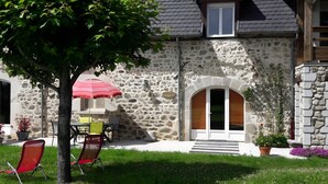 A stone building with a door, a window, and a small outdoor seating area with chairs and a table. - Holiday Home 'Gîte Le Rosier' with Wi-Fi (Saint-Mamet-la-Salvetat)