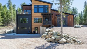 Een modern meerlaags huis met een houten gevel, grote ramen en een stenen fundering.
