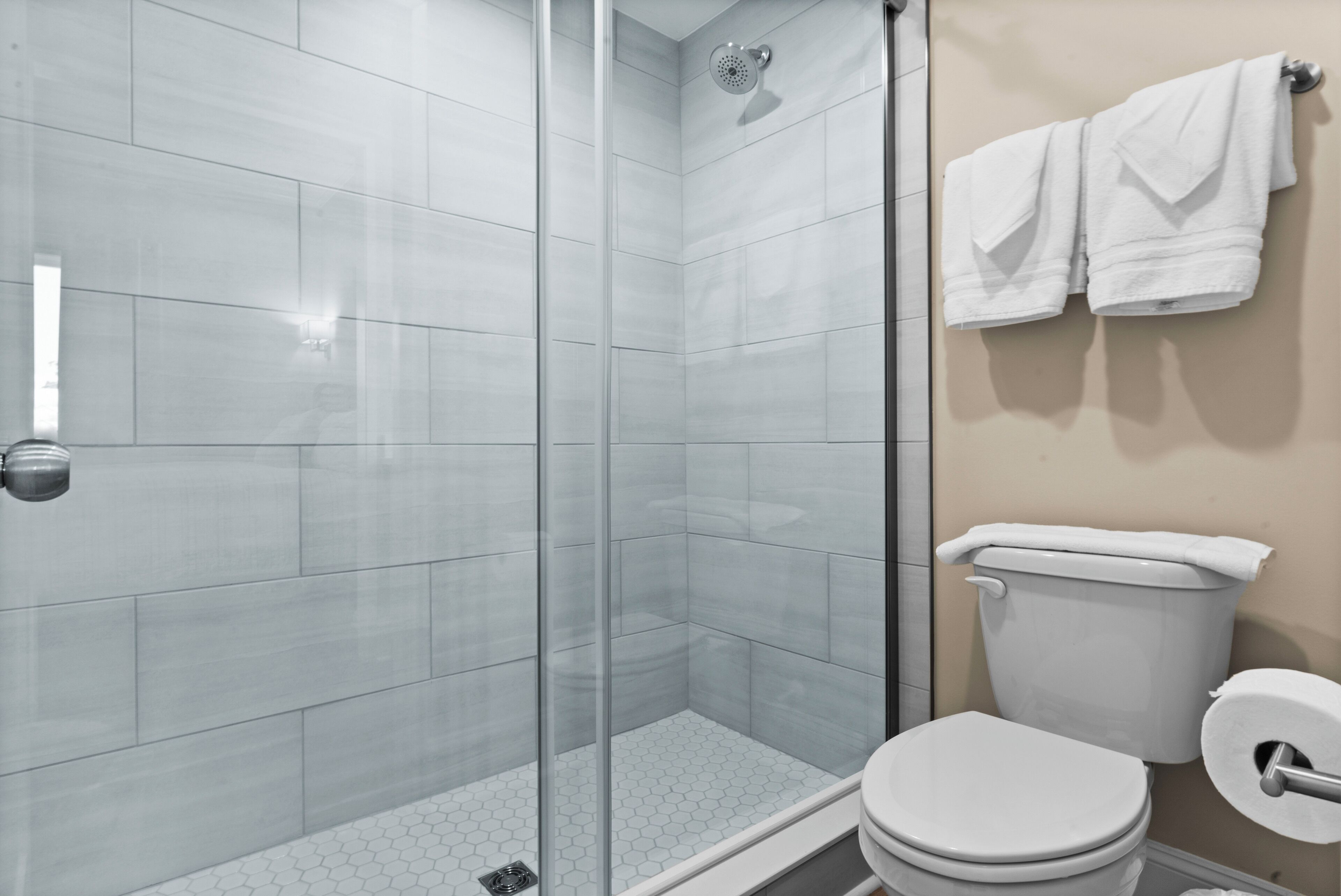 Une salle de bain moderne avec une douche à parois de verre, des toilettes et deux serviettes blanches suspendues à un porte-serviettes.