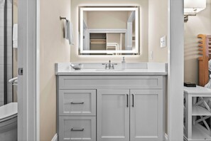 A bathroom with a white vanity, a mirror with built-in lighting, and a toilet.