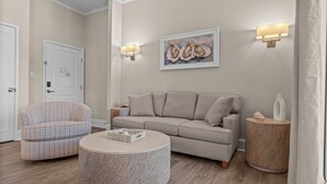 Un salon avec un canapé beige, un fauteuil à motifs, une table basse ronde et deux lampes fixées au mur.