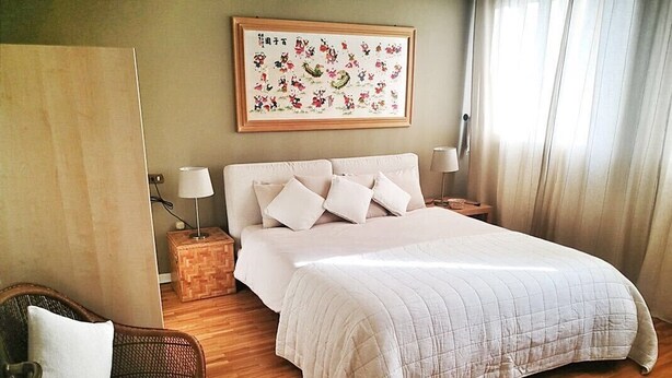 A bedroom with a large bed, a wooden floor, a wicker chair, and a framed artwork on the wall. - JESOLO LIDO AT 300 Mt FROM THE BEACH (Lido di Jesolo)