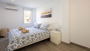 A bedroom with a bed, a bedside table, a nightstand, a window, and an air conditioning unit. - Javea Apartment 300 meters from sandy beach and many bars/restaurants (javea)