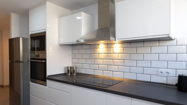 A modern kitchen with white cabinetry, stainless steel appliances, and a black countertop. - Javea Apartment 300 meters from sandy beach and many bars/restaurants (javea)