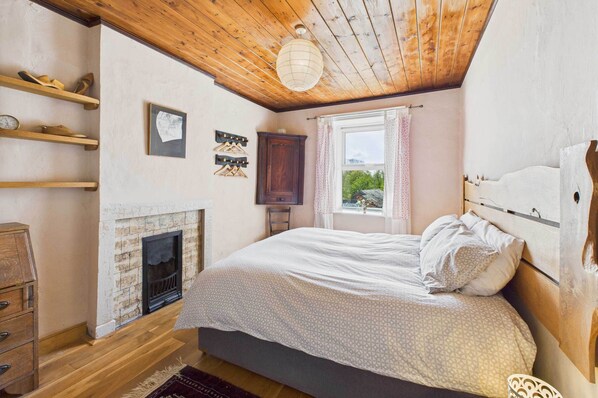 Une chambre avec un plafond en bois, une cheminée, un lit avec une tête de lit et une fenêtre avec des rideaux.