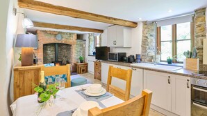 A cozy kitchen with stone walls, wooden beams, a fireplace, and a dining area set for a meal.