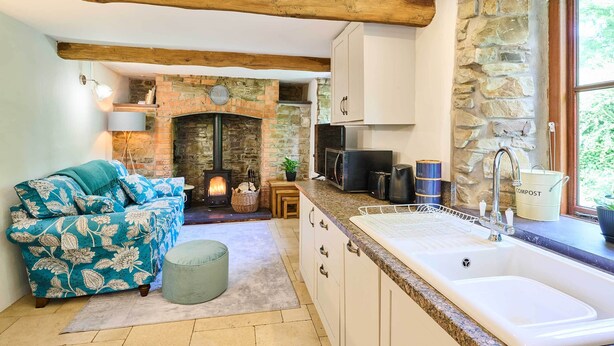 A cozy kitchen with a stone fireplace, a sofa with floral upholstery, and a sink with a compost bin.