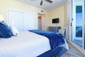 Une chambre à coucher comprenant un lit, une commode, un téléviseur et une porte-fenêtre coulissante donnant sur un balcon.