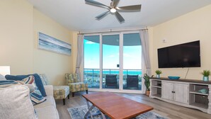 A living room with a sofa, a coffee table, a TV, and a balcony with a view of the ocean.