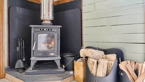 A wood-burning stove with logs and a pot nearby. - Host & Stay | Dipple Farm Shepherds Hut (Woolfardisworthy)