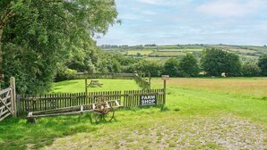 A rural landscape with a wooden gate labeled "FARM SHOP" and a wooden cart. - Host & Stay | Dipple Farm Shepherds Hut (Woolfardisworthy)