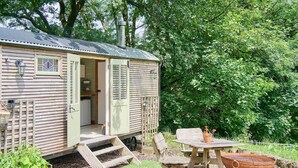 A mobile home with a kitchen area, a dining table with chairs, a grill, and a small garden area with plants. - Host & Stay | Dipple Farm Shepherds Hut (Woolfardisworthy)