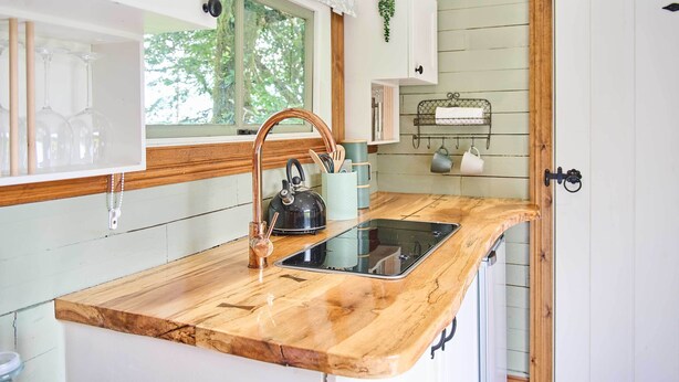 A kitchen with a wooden countertop, a black kettle, and a window with a view of trees. - Host & Stay | Dipple Farm Shepherds Hut (Woolfardisworthy)
