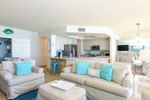 Ein modernes Wohnzimmer mit einer Couch, einem Hocker und einer Küche im Hintergrund.