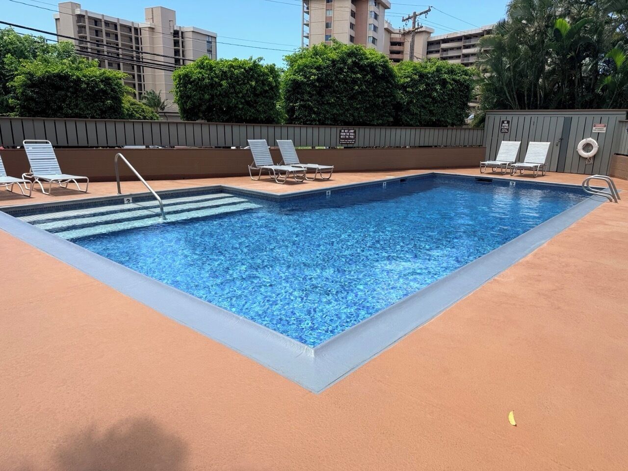 Una piscina rettangolare con interni blu, circondata da un solarium color beige. Si vedono lettini e una postazione di salvataggio.