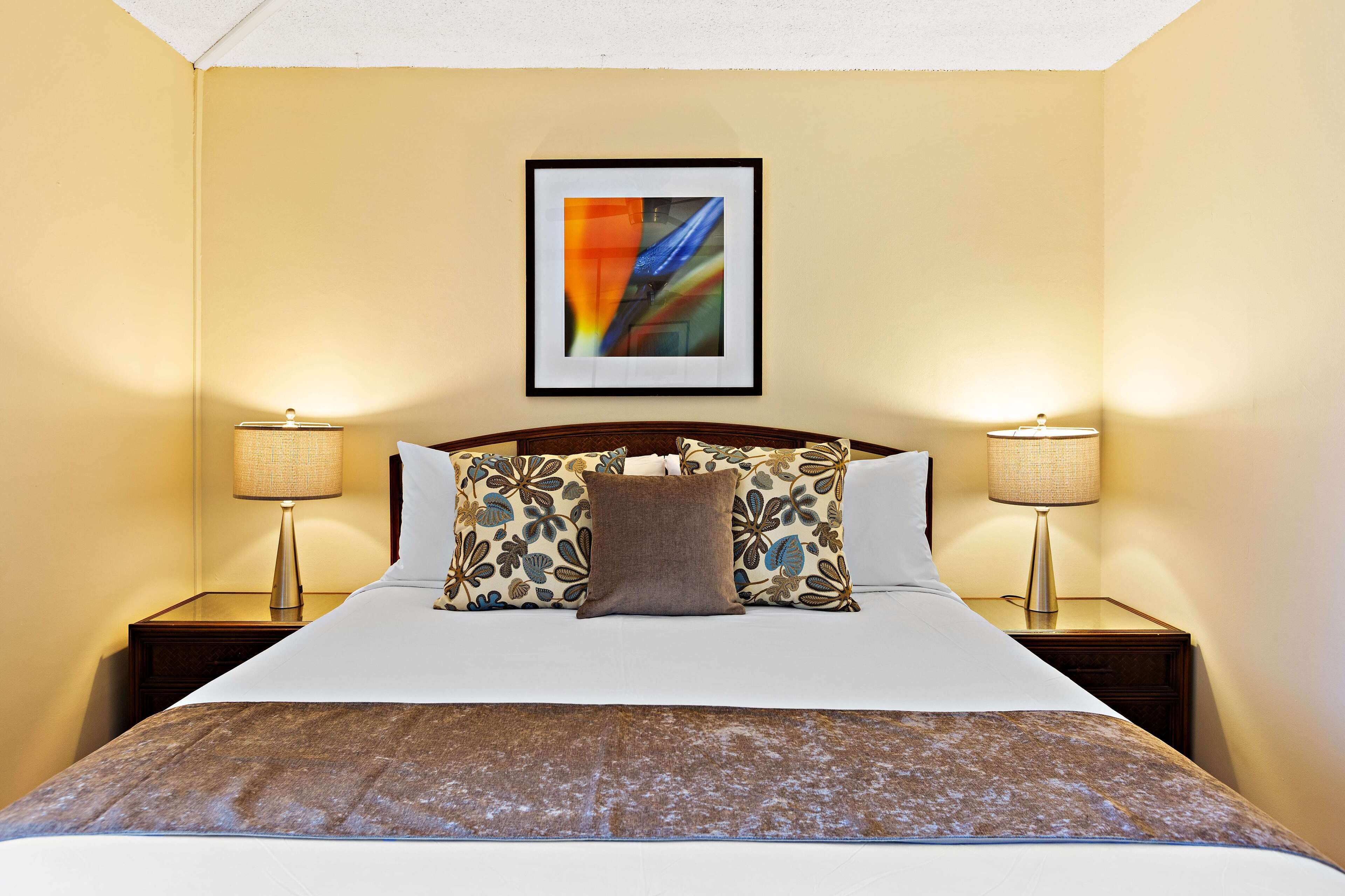 A hotel room with a large bed, two bedside tables with lamps, and a framed abstract painting on the wall.