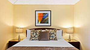 Ein Hotelzimmer mit einem großen Bett, zwei Nachttischen mit Lampen und einem gerahmten abstrakten Gemälde an der Wand.