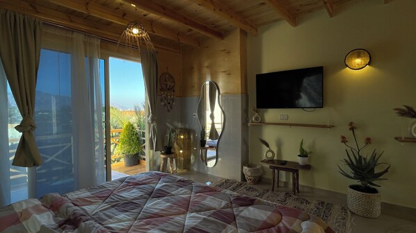Ein Schlafzimmer mit einem großen Bett, einem an der Wand montierten Fernseher und einem Balkon mit Pflanzen.
