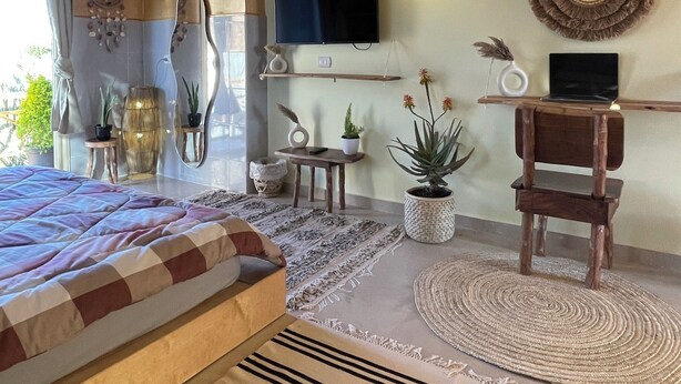 Un dormitorio acogedor con cama, vigas de madera en el techo, televisor, computadora portátil y varios objetos decorativos.