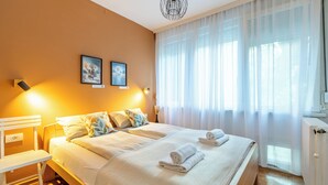 A hotel room with a large bed, two bedside tables, a chair, and a window with sheer curtains.